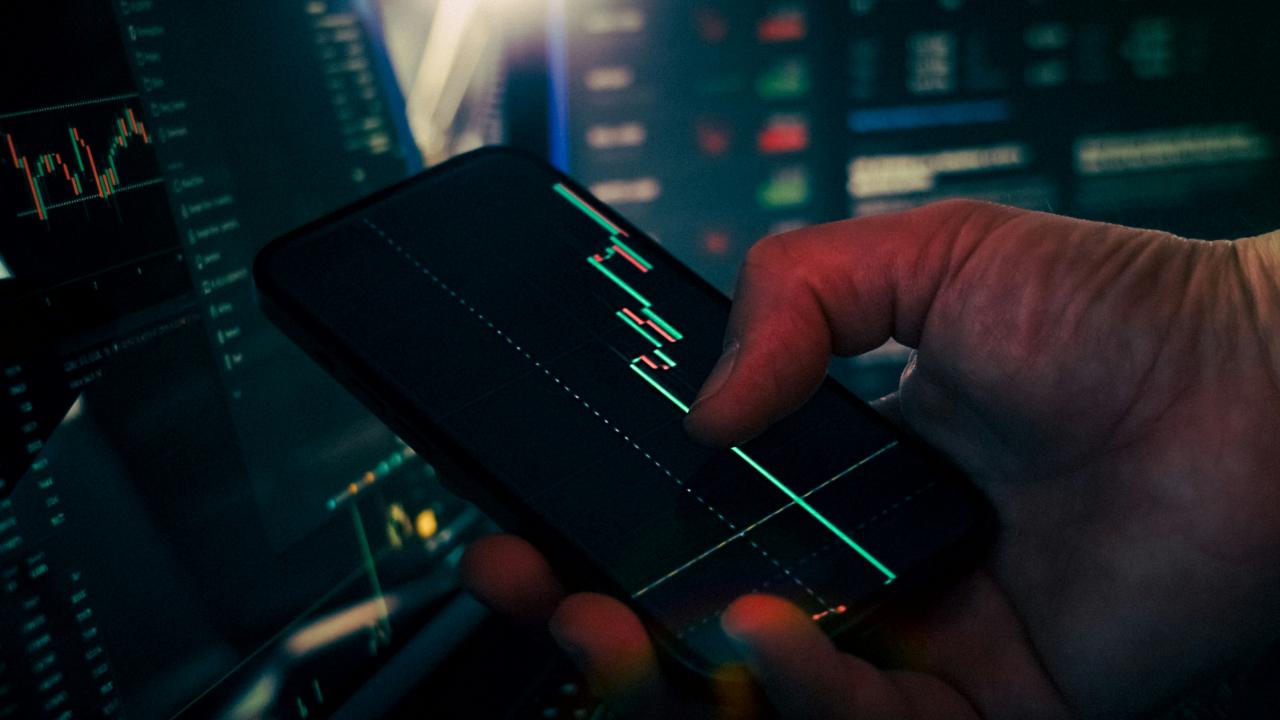 Trader menganalisis data pasar saham di smartphone dan ponsel
