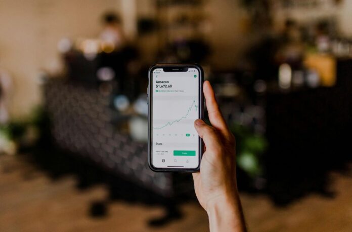 orang yang memegang iPhone hitam menampilkan bursa saham