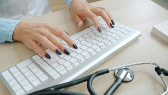Dokter mengetik di keyboard dengan stetoskop di dekatnya