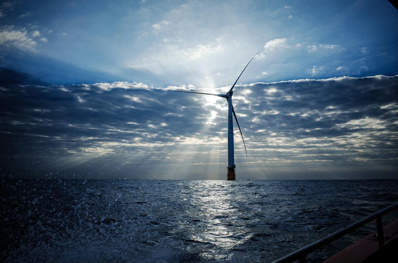 Sebuah turbin angin tunggal berdiri di laut saat matahari terbenam.